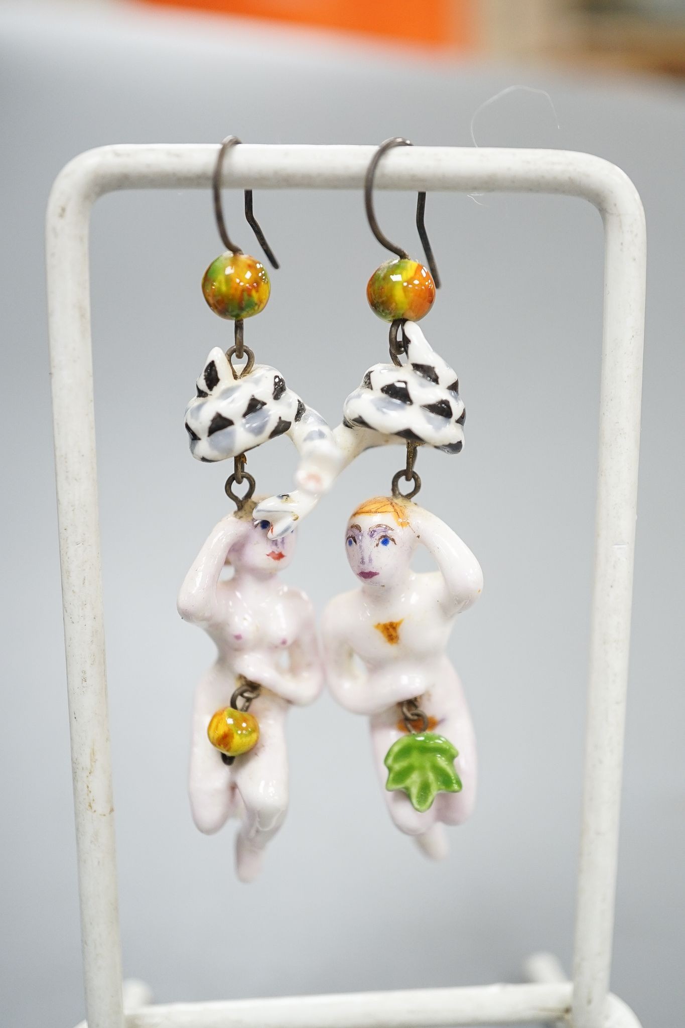 A pair of painted porcelain 'Adam & Eve with serpent' drop earrings, 62mm